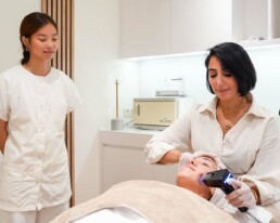 Praticienne utilisant un appareil de soin sur une cliente allong&eacute;e, une seconde praticienne &agrave; ses c&ocirc;t&eacute;s, chez About Your Skin &agrave; Bruxelles