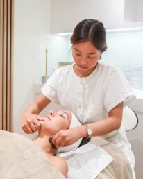 Praticienne r&eacute;alisant un massage du visage sur une cliente allong&eacute;e, en cabine de soin chez About Your Skin, avenue Louise &agrave; Bruxelles