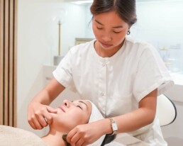 Praticienne r&eacute;alisant un massage du visage sur une cliente allong&eacute;e, en cabine de soin chez About Your Skin, avenue Louise &agrave; Bruxelles