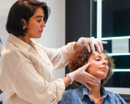 Praticienne examinant la peau du visage d'une cliente assise devant le miroir, chez About Your Skin &agrave; Bruxelles