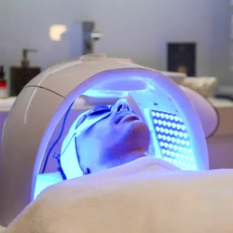 Cliente allongée sous un masque LED bleu lumineux, chez About Your Skin à Bruxelles