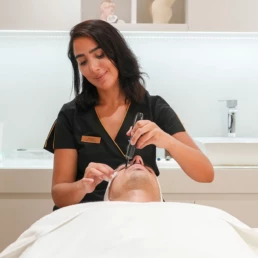 Praticienne appliquant un soin au stylet fin sur le front d'un client allongé, chez About Your Skin à Bruxelles