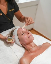 Praticienne appliquant un soin actif à la main sur le front d'une cliente allongée, chez About Your Skin à Bruxelles
