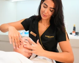 esth&eacute;ticienne r&eacute;alisant un massage de drainage lymphatique du visage sur une cliente, mains pos&eacute;es le long de la m&acirc;choire