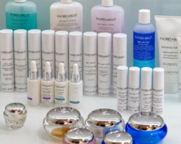 Gamme de soins Ingrid Millet : flacons, s&eacute;rums et pots de cr&egrave;me align&eacute;s sur un plan blanc